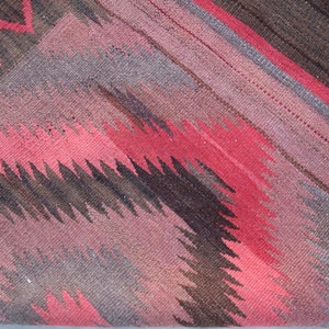 May include: A close-up of a woven rug with a geometric pattern in shades of red, brown, and gray.