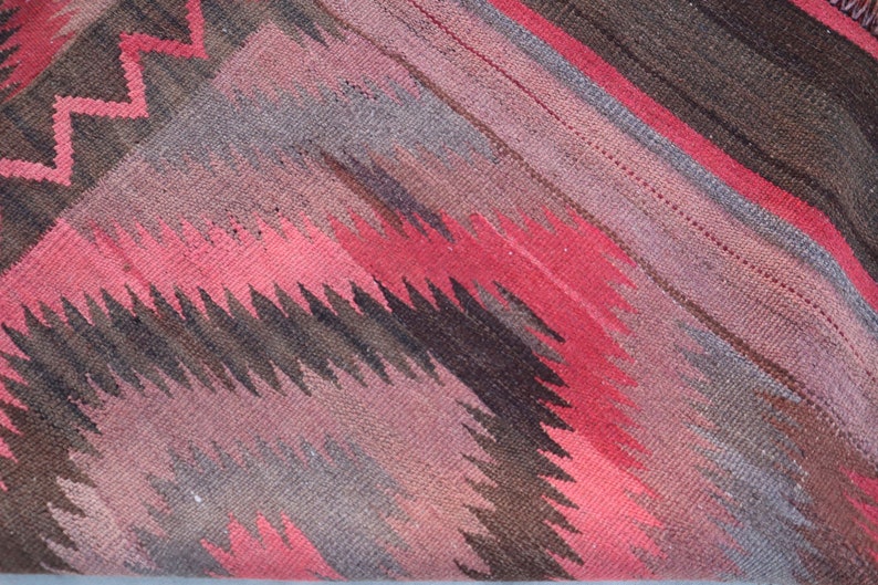 May include: A close-up of a woven rug with a geometric pattern in shades of red, brown, and gray.