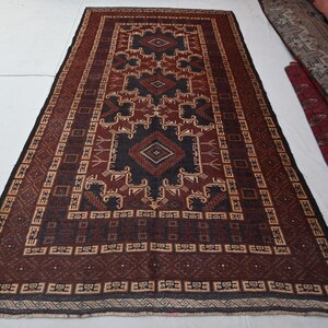 May include: A rectangular, hand-woven rug with a central geometric design in black, brown, and beige. The rug features a repeating border pattern and is displayed on a white surface. The rug's dimensions are not visible.