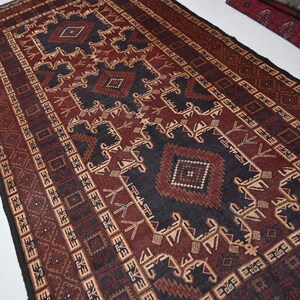May include: A rectangular rug with a geometric pattern in shades of burgundy, black, and beige. The rug features repeating diamond and stylized floral motifs, creating a traditional, textured appearance. The rug's design is symmetrical, with a central medallion and border.