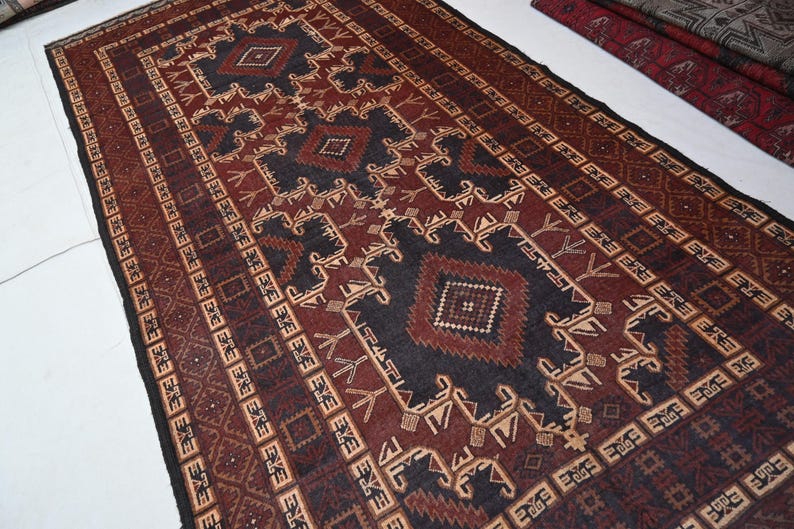 May include: A rectangular rug with a geometric pattern in shades of burgundy, black, and beige. The rug features repeating diamond and stylized floral motifs, creating a traditional, textured appearance. The rug's design is symmetrical, with a central medallion and border.