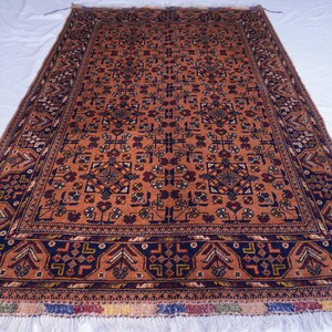 May include: An orange and navy rectangular rug with an intricate geometric pattern. The rug has a dark navy border with repeating shapes and a fringed edge. The central design features repeating floral and geometric motifs.
