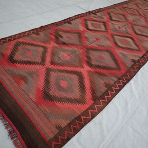 May include: A long, rectangular rug with a geometric pattern in shades of red, brown, and gray. The rug has a fringe border.