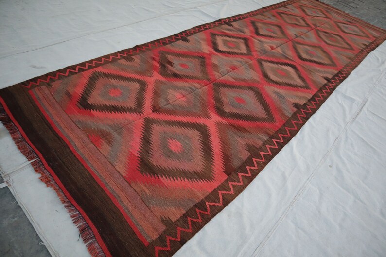 May include: A long, rectangular rug with a geometric pattern in shades of red, brown, and gray. The rug has a fringe border.