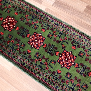May include: A green runner rug with a traditional Persian design featuring red and black accents. The rug has a geometric pattern with intricate details.