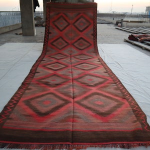 May include: A long, red and brown rug with a geometric diamond pattern. The rug is folded in half and laid out on a white surface.
