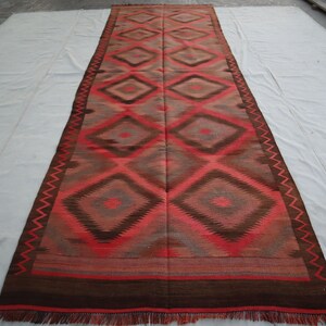 May include: A long, rectangular rug with a geometric pattern of diamonds in shades of red, brown, and gray. The rug has a fringe border.