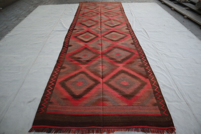 May include: A long, rectangular rug with a geometric pattern of diamonds in shades of red, brown, and gray. The rug has a fringe border.