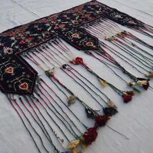 Puede incluir: Textil azul oscuro adornado con intrincados patrones florales y geom&eacute;tricos. El textil presenta m&uacute;ltiples secciones con largas borlas decorativas en varios colores, incluyendo rojo, blanco y verde. El dise&ntilde;o es sim&eacute;trico y detallado.