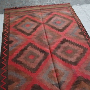 May include: A red, brown, and gray patterned rug with a geometric design. The rug has a fringe border.