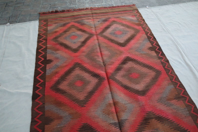 May include: A red, brown, and gray patterned rug with a geometric design. The rug has a fringe border.