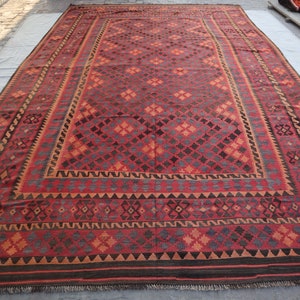 May include: A traditional red, orange, and black patterned rug with a geometric design. The rug has a fringe border.