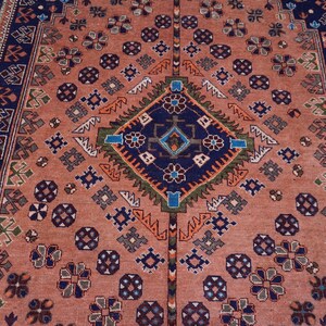 May include: A detailed, rectangular rug with a central diamond pattern in navy blue, green, and orange. The rug features a salmon-colored field with repeating floral and geometric motifs, and a navy blue border.