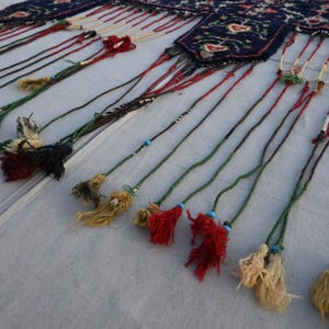 Puede incluir: Primer plano de un textil decorativo con una parte superior estampada en azul oscuro y largas y coloridas borlas. Las borlas son de varios colores, incluyendo rojo, verde y amarillo, con peque&ntilde;as cuentas. El textil se utiliza probablemente para la decoraci&oacute;n del hogar.