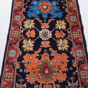 May include: A rectangular, patterned rug with a dark blue background. The rug features a central design in orange, blue, yellow, and green, with a red border. The rug's design includes floral and geometric elements.