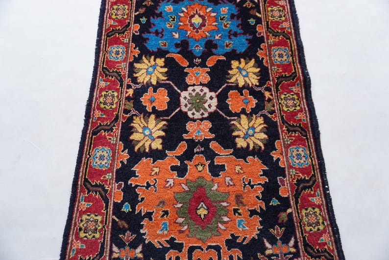 May include: A rectangular, patterned rug with a dark blue background. The rug features a central design in orange, blue, yellow, and green, with a red border. The rug's design includes floral and geometric elements.