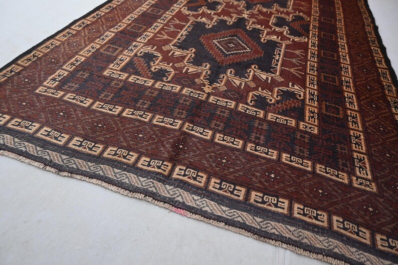 May include: A rectangular, hand-woven rug with a geometric pattern. The rug features a central diamond design in dark brown and black, surrounded by repeating patterns in beige and brown. The border is a darker shade of brown with geometric shapes.