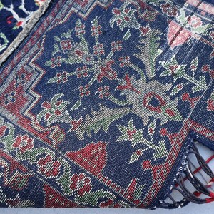 K&ouml;nnte beinhalten: Nahaufnahme eines Teils eines dunkelblauen Teppichs mit einem Blumenmuster in Rot, Gr&uuml;n und Wei&szlig;. Der Teppich hat einen detaillierten Rand und Fransen. Der Teppich ist gefaltet und zeigt die Unterseite.