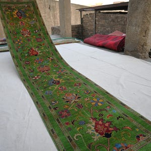 May include: A green and red patterned rug with floral designs. The rug is laid out on a white surface.