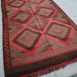 May include: A red, brown, and gray patterned rug with a geometric design. The rug has a fringe border.
