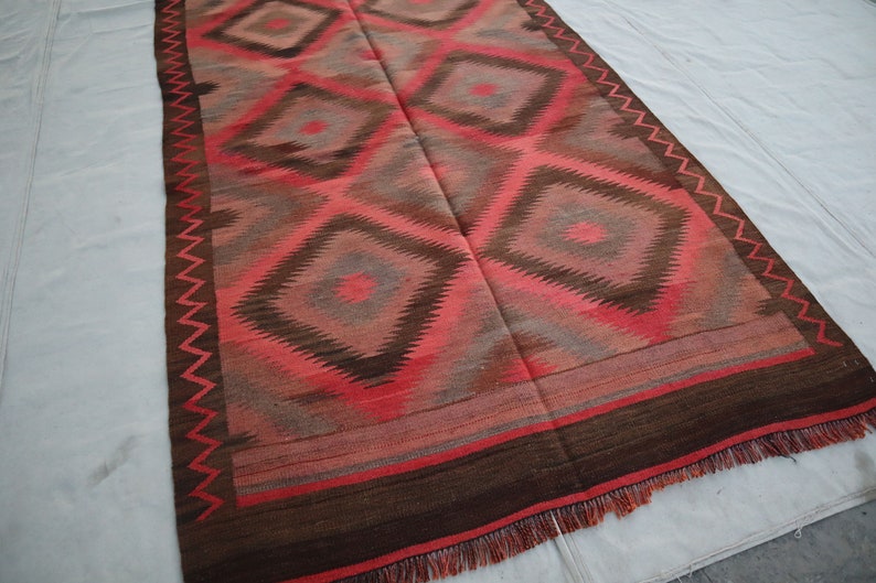 May include: A red, brown, and gray patterned rug with a geometric design. The rug has a fringe border.
