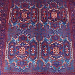 May include: A rectangular, patterned rug with a central design in shades of blue, red, and cream. The rug features an intricate, symmetrical pattern with floral and geometric elements. The border is a darker blue with repeating geometric shapes.