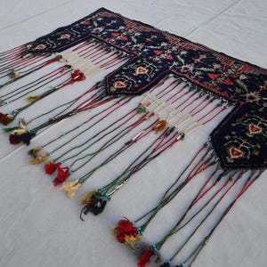 Puede incluir: Textil azul oscuro con un estampado floral y detalles rojos. El textil tiene m&uacute;ltiples borlas en varios colores, incluyendo rojo, verde y crema. Las borlas est&aacute;n unidas al borde inferior del textil.