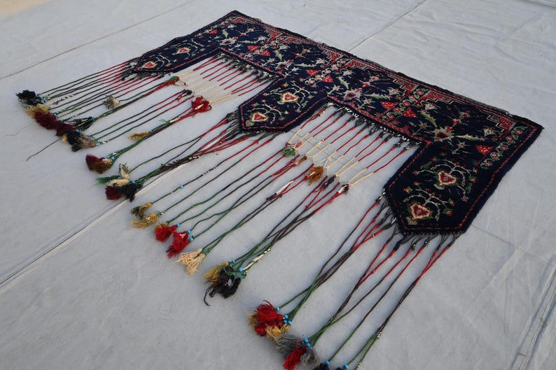 Puede incluir: Textil azul oscuro con un estampado floral y detalles rojos. El textil tiene m&uacute;ltiples borlas en varios colores, incluyendo rojo, verde y crema. Las borlas est&aacute;n unidas al borde inferior del textil.