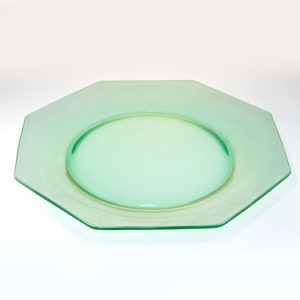 May include: A light green, octagonal glass plate with a circular center. The plate has a smooth, transparent surface and is set against a white background. The plate is likely for serving food.