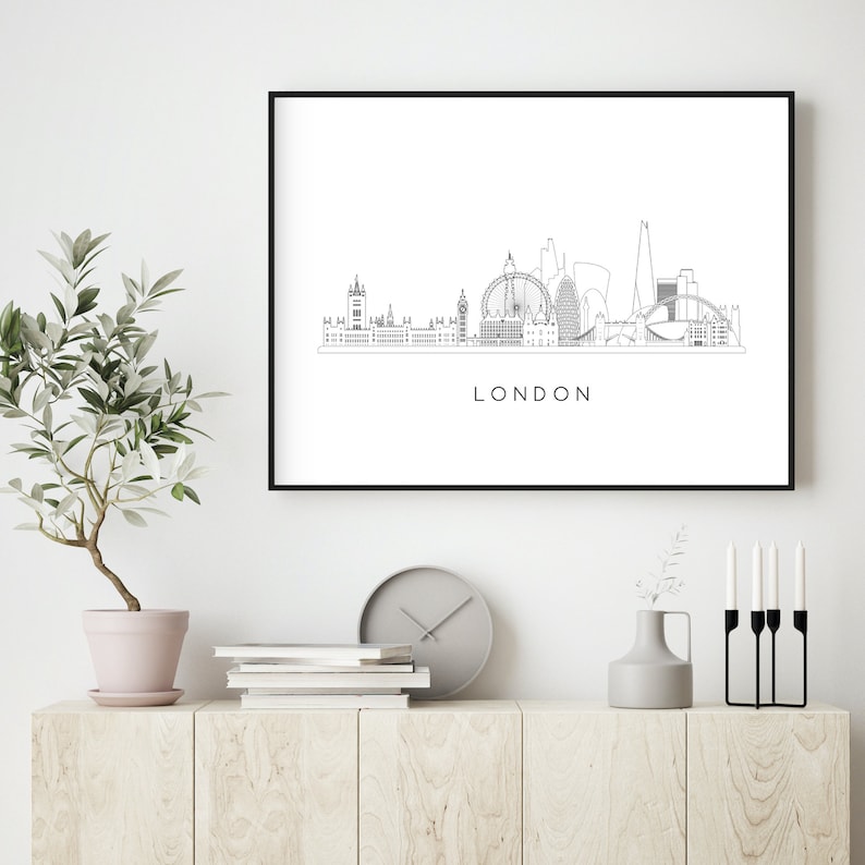 May include: Black and white line art print of the London skyline with the text "LONDON" below the image. The print is framed in a black frame and is hanging on a white wall.