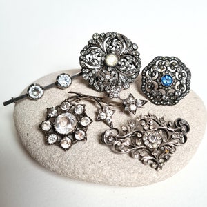 Peut inclure: Une collection de broches vintage en argent avec des strass clairs et bleus. Les broches sont disposées sur une pierre de couleur gris clair.