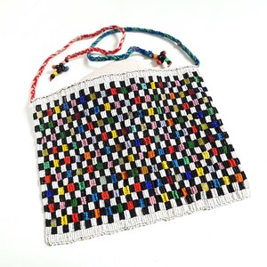 Könnte beinhalten: Eine kleine, bunte Perlen-Tasche mit einem karierten Muster. Die Tasche hat einen langen Riemen aus rotem, weißem und blauem Garn.