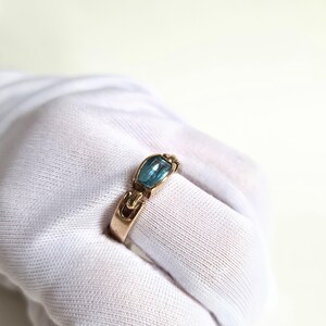 May include: A gold-toned ring featuring a rectangular, light blue gemstone. The ring has a unique design with curved accents on the band and around the stone. The gemstone is set in a bezel setting, enhancing its color and shape. A piece of jewelry.