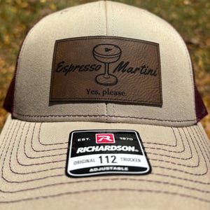 May include: A beige and maroon trucker hat with a brown leather patch that says "Espresso Martini" and "Yes, please." The hat is made by Richardson and has a size tag that says "112".