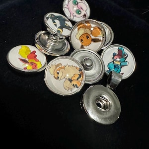 Może przedstawiać: Zestaw 10 kolorowych guzików z postaciami Pokemon. Guziki są okrągłe i mają srebrne metalowe plecy. Postacie obejmują Pikachu, Eevee, Charmandera, Squirtle'a, Bulbasaura i wiele innych.