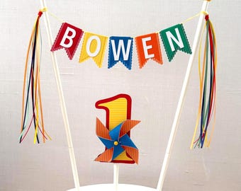 Personalized cake topper with name in colorful primary colors + orange with center number and mini pinwheel