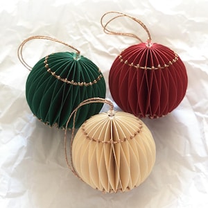 May include: Three decorative paper ornaments in green, red, and beige. Each sphere has a pleated design and is adorned with gold-colored string and a loop for hanging. These ornaments are ideal for holiday or seasonal decor.