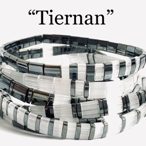 May include: Stack of four bracelets, two black and white and two black. The bracelets are made of square beads.