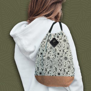 Puede incluir: Una bolsa de cordón blanco con un estampado celestial en blanco y negro. La bolsa tiene un fondo marrón y una pequeña etiqueta negra con el texto "Astrological" y "Soul Bag".