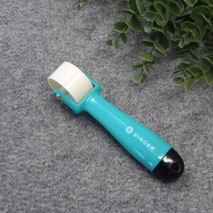 May include: A turquoise blue seam roller with a white roller and a black handle. The handle has the word "SINGER" printed on it.