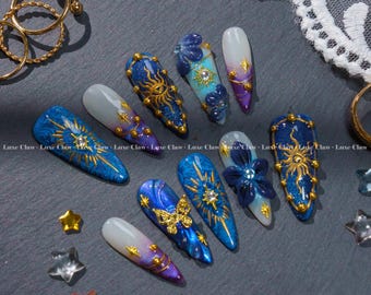 May include: A selection of long, almond-shaped artificial nails with detailed designs. The nails showcase celestial themes with gold suns, stars, and butterflies on a blue, purple, and white gradient. Some nails have 3D floral decorations.