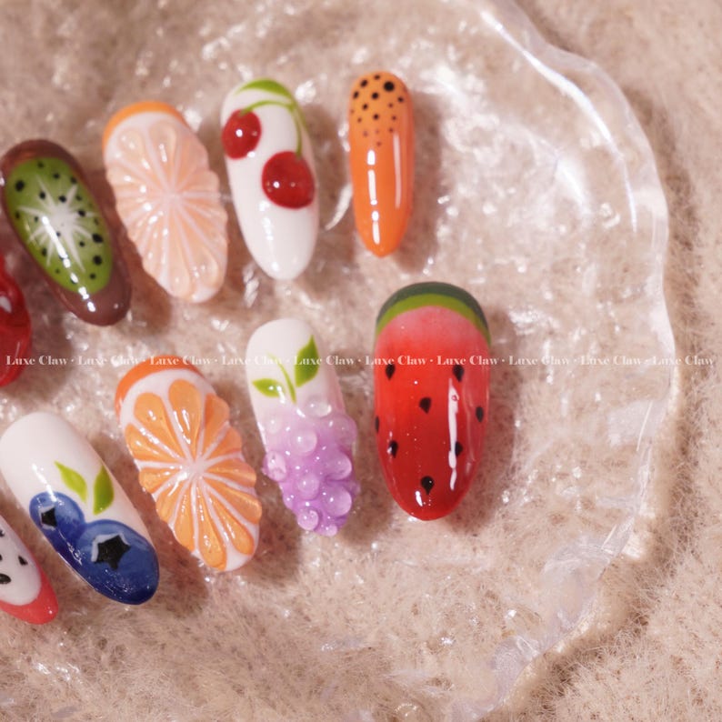 May include: A set of ten fake nails with different fruit designs. The nails are painted with various fruits, including kiwi, orange, cherry, watermelon, grapes, and blueberries.