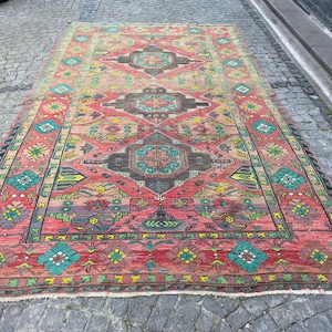 May include: A vintage Turkish rug with a colourful geometric pattern in shades of red, green, blue, and yellow. The rug has a fringed edge and is laid out on a cobblestone surface.