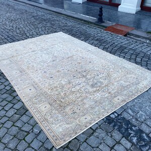 May include: A large, off-white rug with a floral pattern and a border. The rug is laid out on a cobbled surface.