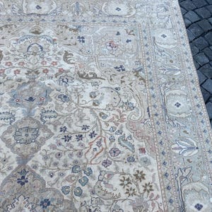 May include: A beige rug with a floral pattern in shades of blue, pink, and brown. The rug has a border with a geometric design.