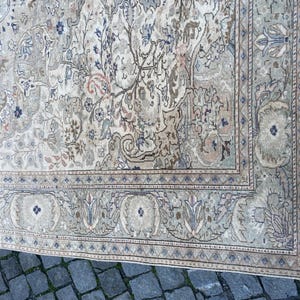 May include: A vintage rug with a cream background and intricate floral patterns in shades of brown, beige, and blue. The rug has a border with a geometric design.