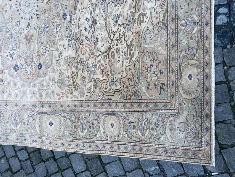 May include: A vintage rug with a cream background and intricate floral patterns in shades of brown, beige, and blue. The rug has a border with a geometric design.