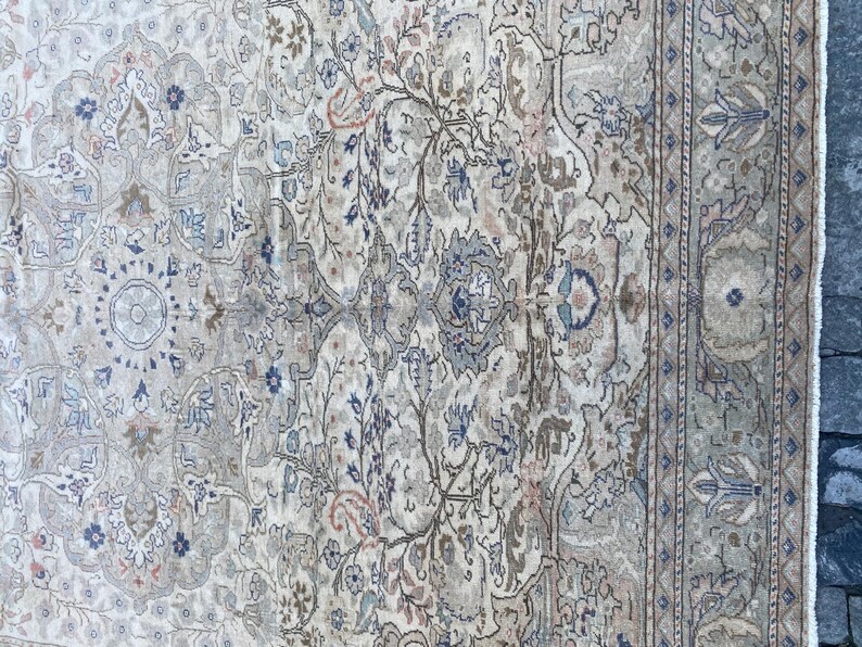 May include: A vintage rug with a beige background and intricate floral patterns in shades of blue, brown, and pink. The rug has a border with a repeating geometric design.