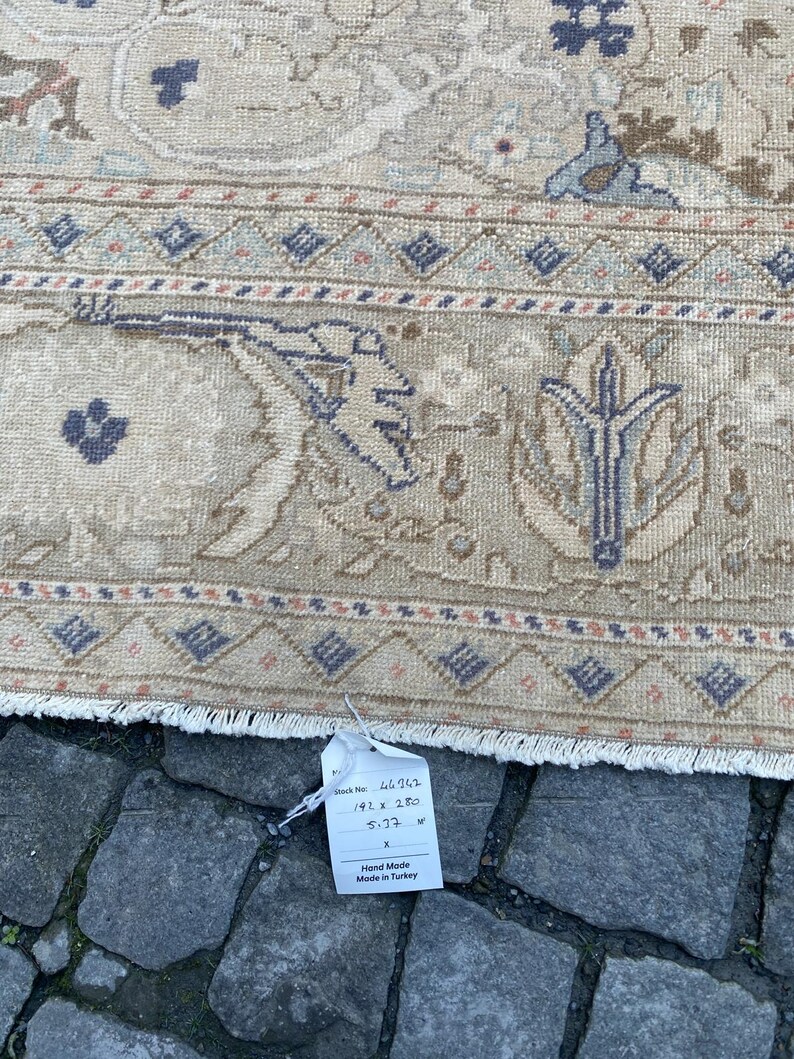 May include: A beige hand-woven rug with a floral pattern in shades of blue, brown, and pink. The rug has a fringe border and a tag that reads "Stock No. 46,962, 192 x 280, 5.73 m2, Hand Made, Made in Turkey."