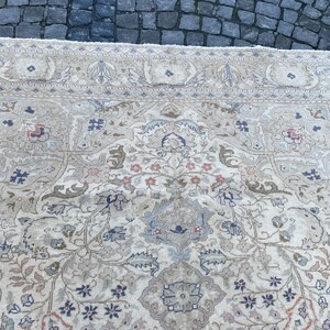 May include: A cream-coloured rug with a floral pattern in shades of blue, pink, and brown. The rug has a border with a repeating design.
